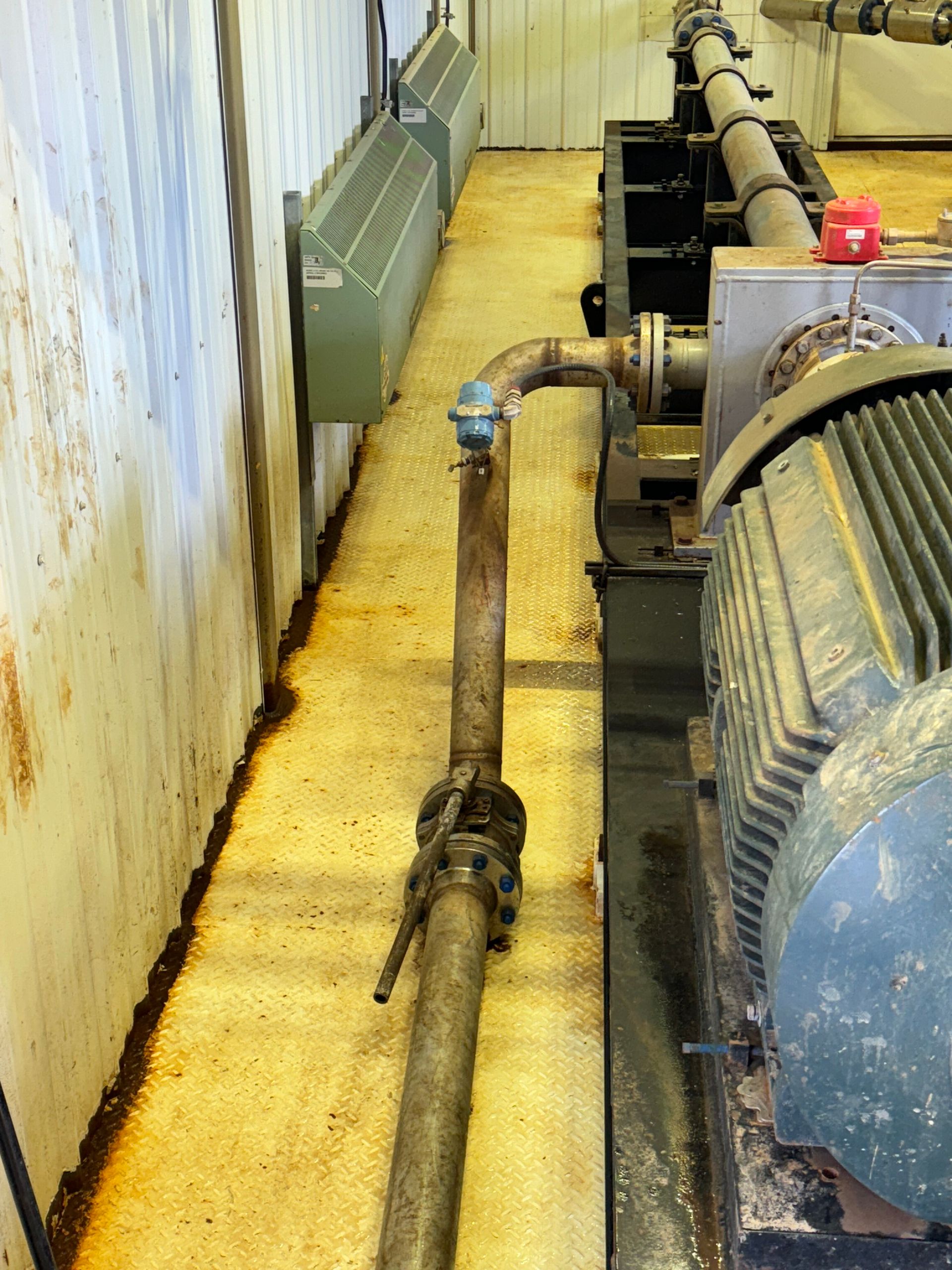 Industrial basement with large pipes and a blue motor along a narrow yellow walkway