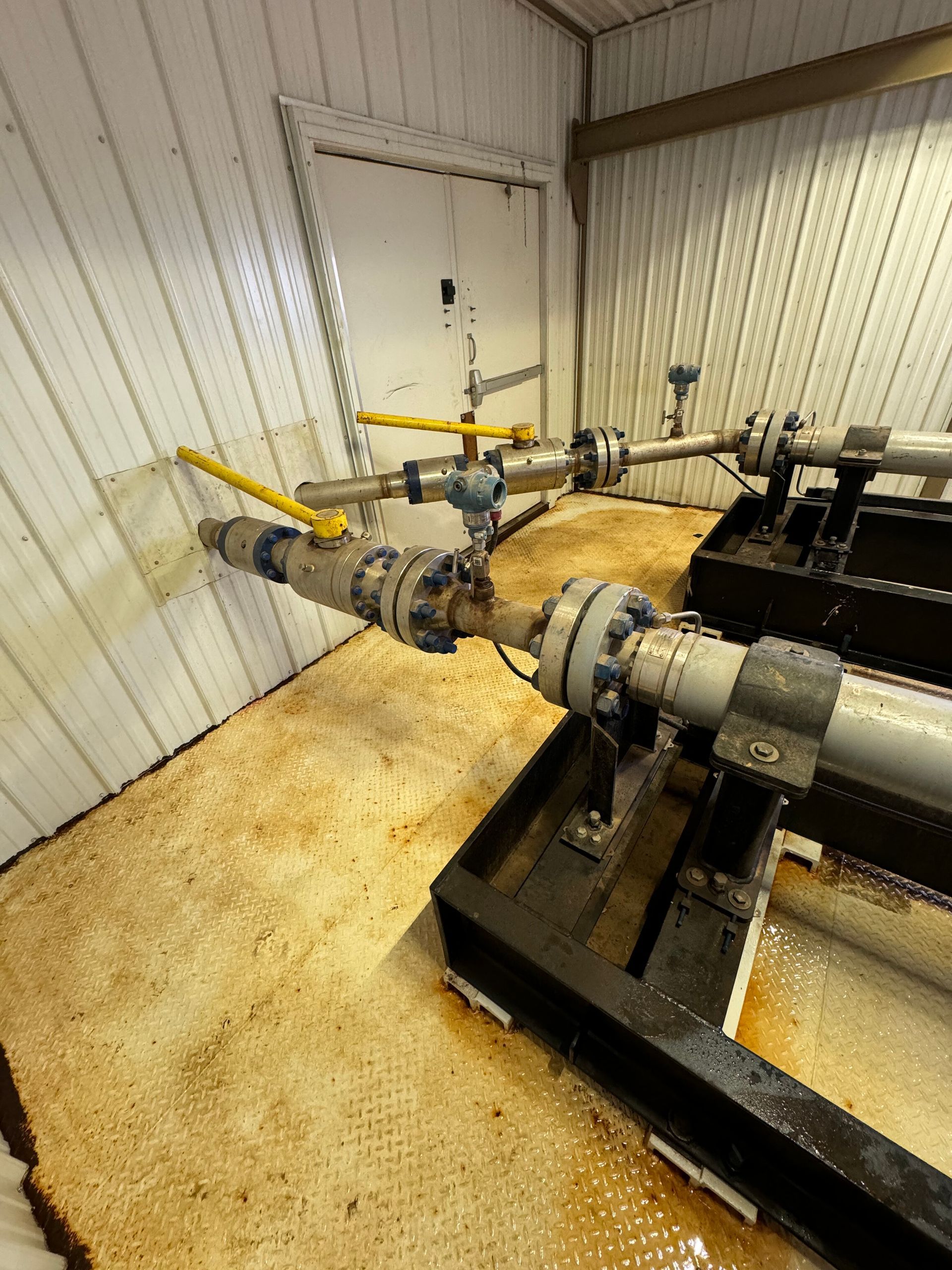 Industrial pipes and valves inside a white utility room, with yellow-handled fittings on the floor.