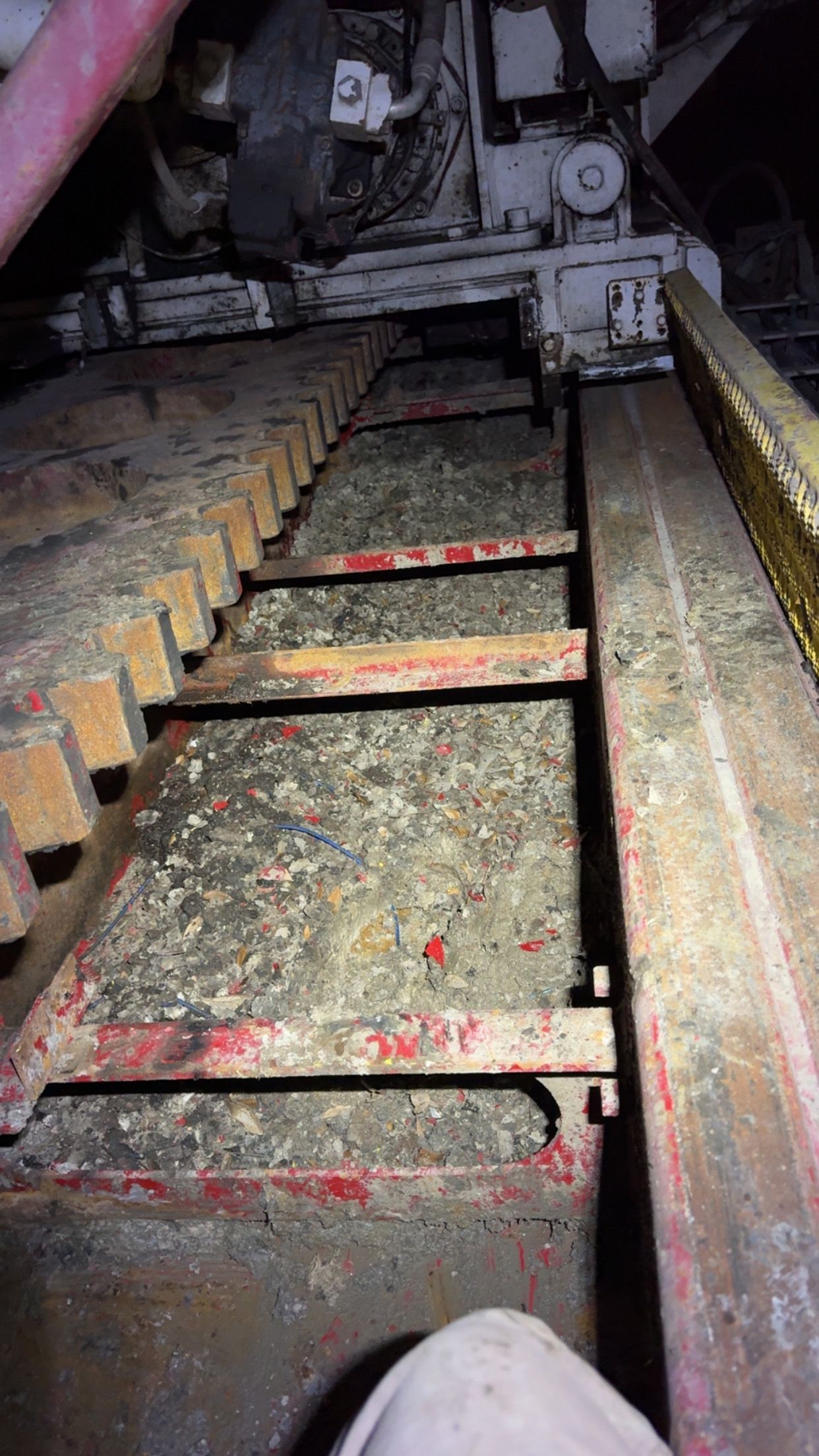 Dirty industrial conveyor with rusted metal slats and debris inside a machine hopper