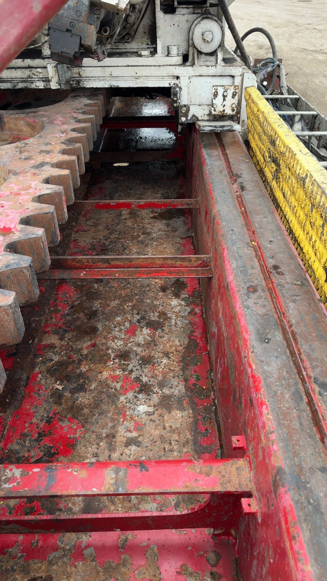 Rusty industrial machinery interior with red rails and a yellow safety guard over a dirty conveyor area