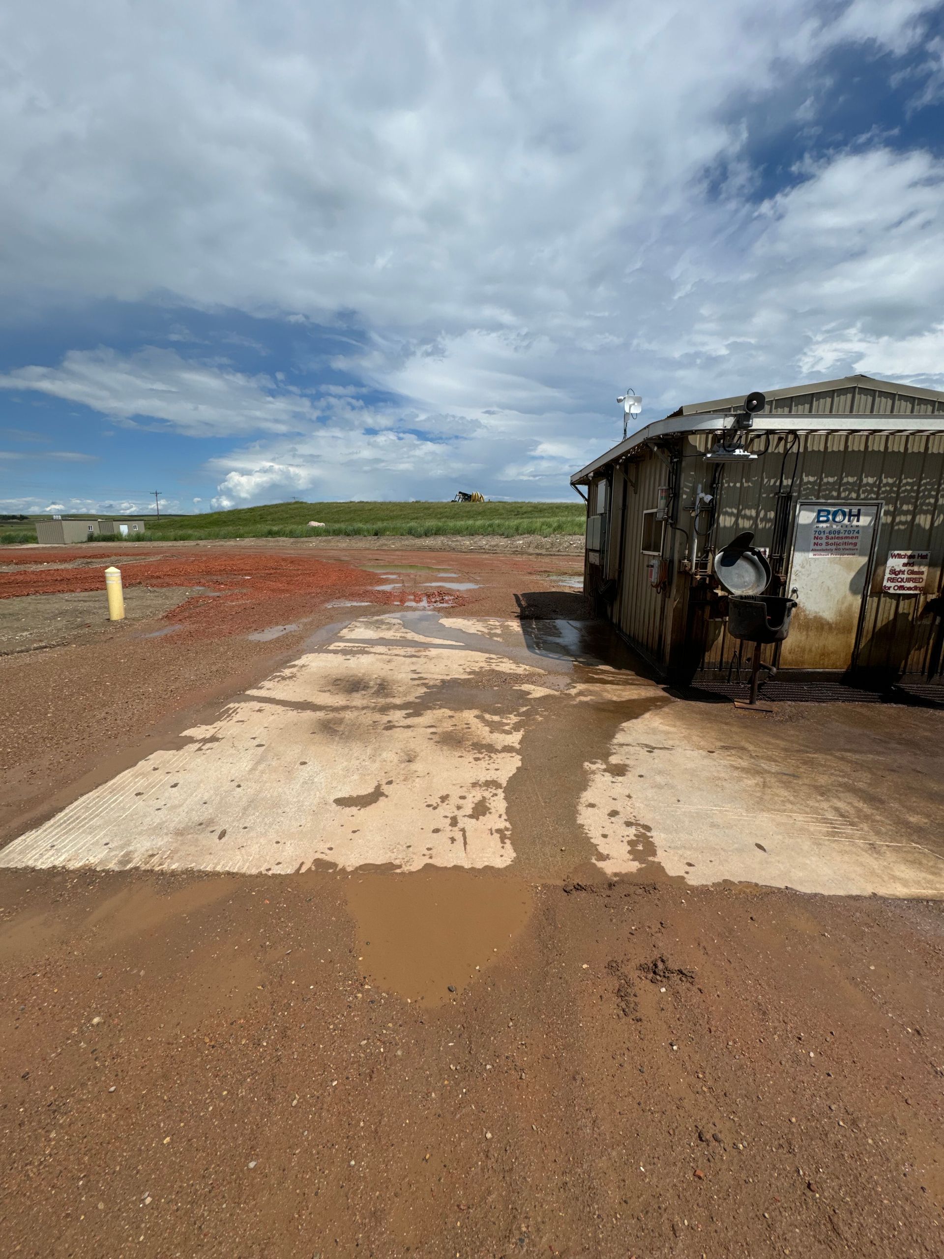 Burnt-out vehicle on a muddy dirt road under a cloudy sky in an open field