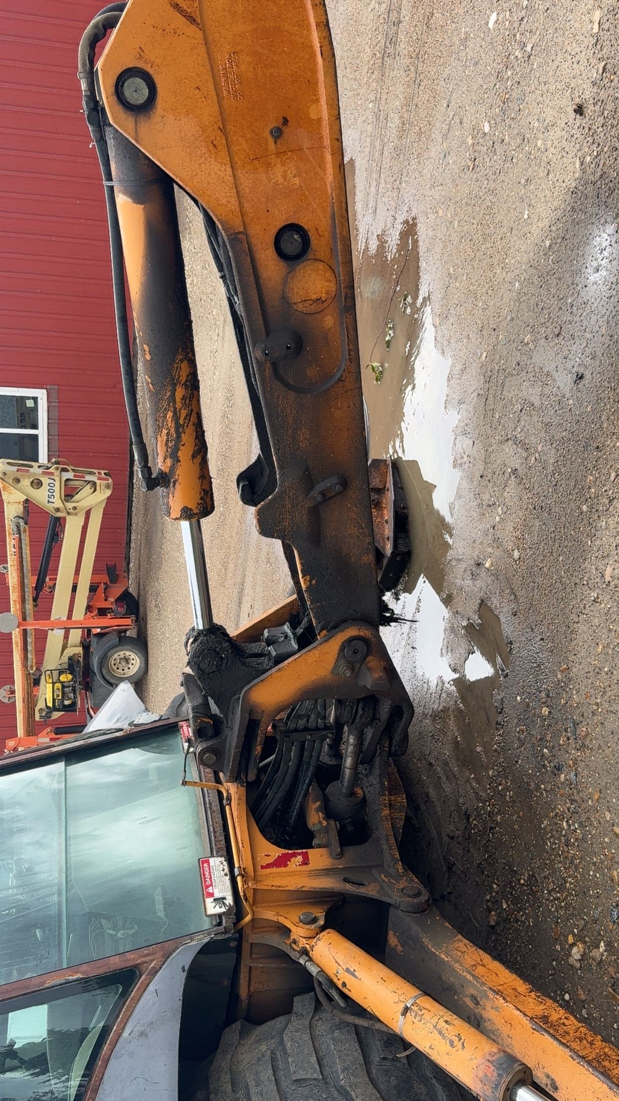 Damaged orange excavator arm with hydraulic components on a construction site, leaning against a wall.