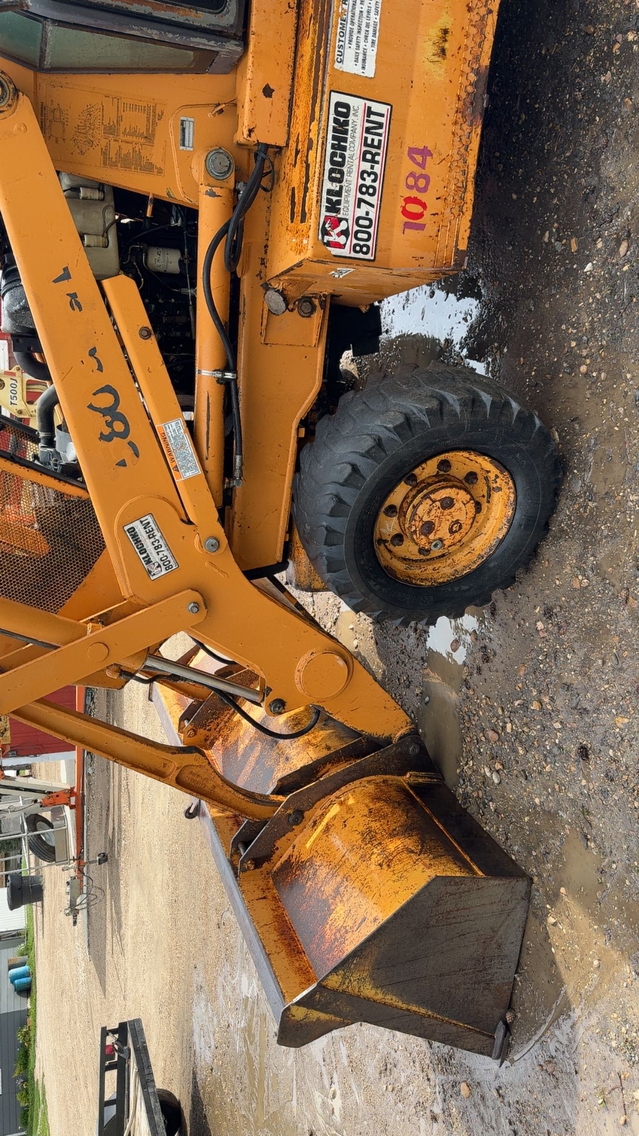 Orange backhoe parked on gravel with a large metal bucket attached