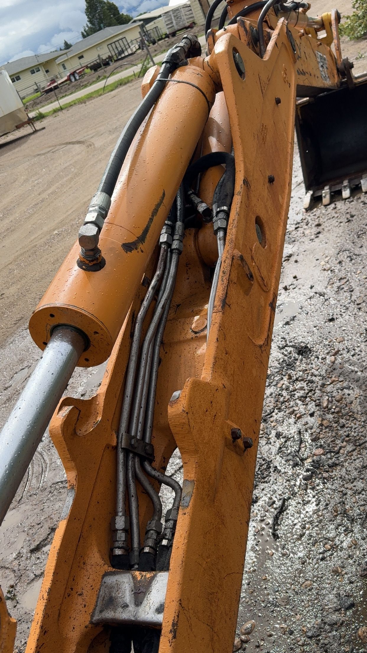 Close-up of an orange excavator arm with hydraulic hoses at a construction site