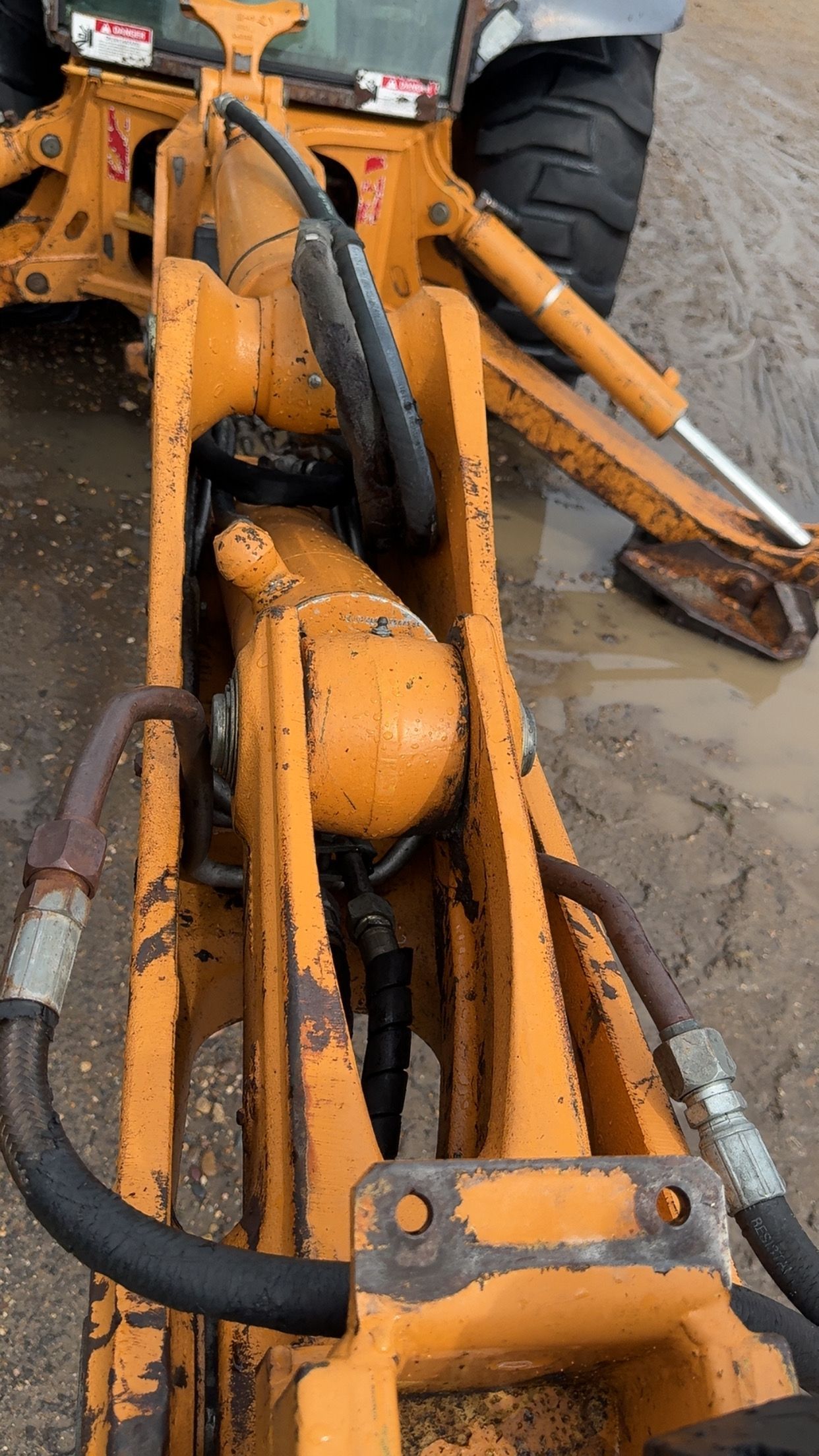 Close-up of an orange construction machine with hydraulic hoses and muddy metal parts on a wet site