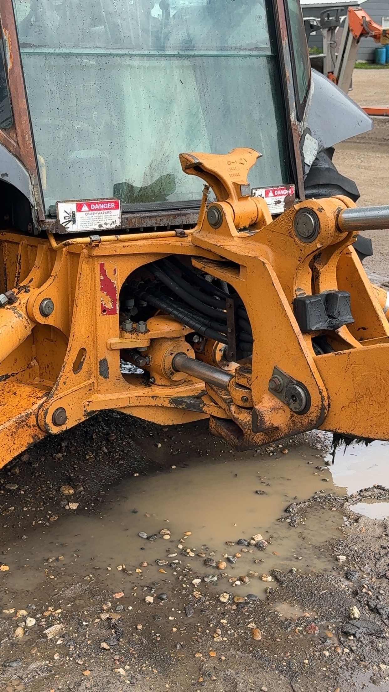 Yellow construction vehicle bucket digging muddy ground beside a wet gravel area