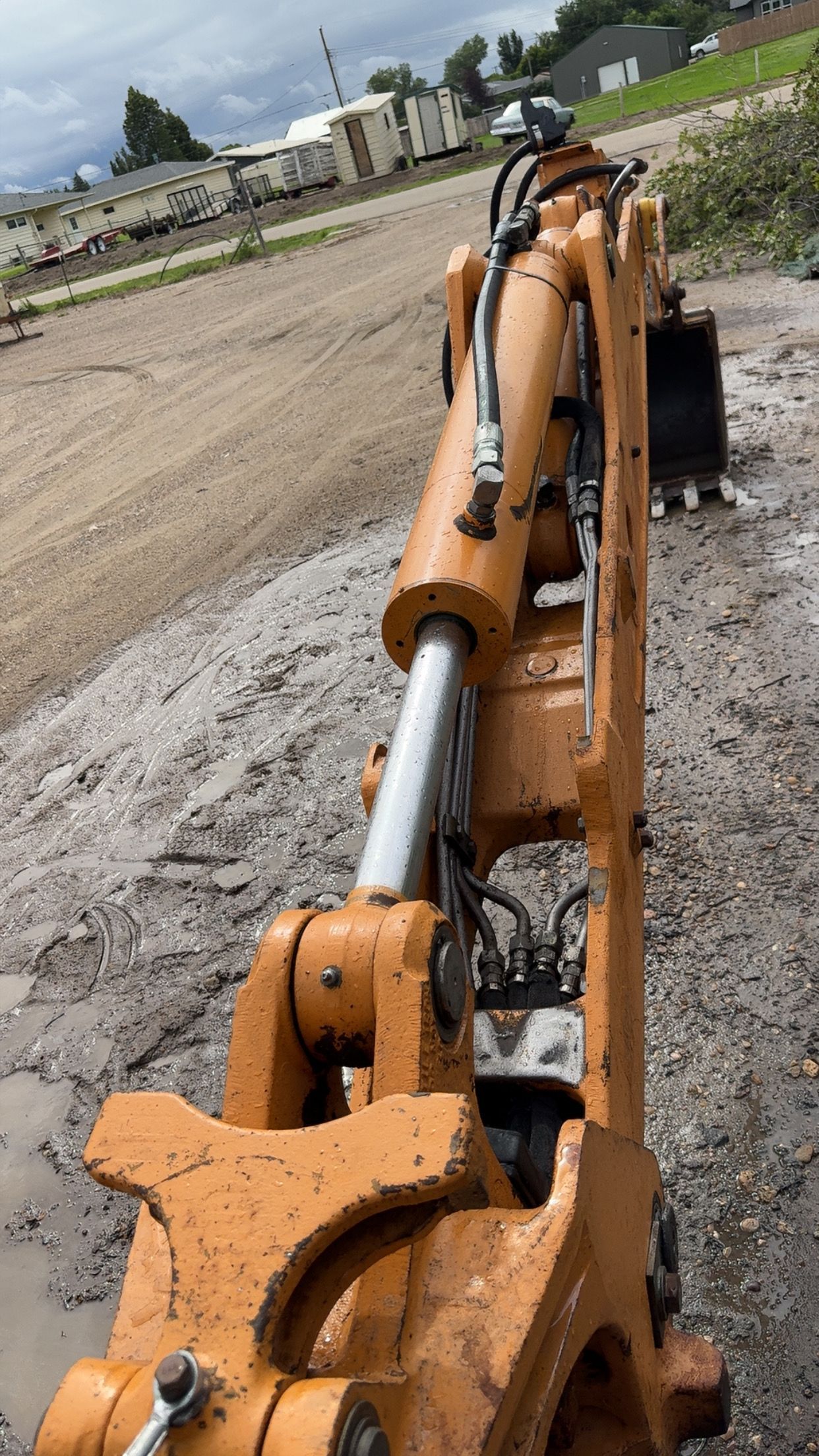 Orange excavator arm and hydraulic cylinder on a muddy construction site.