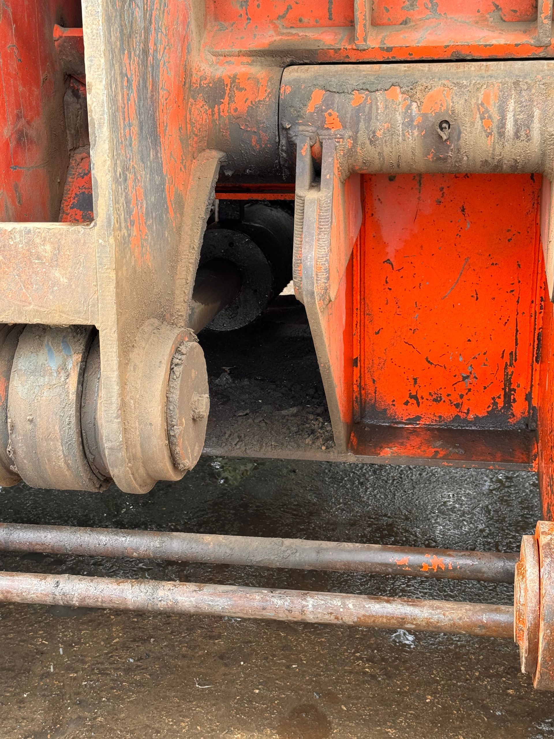 Close-up of rusty orange industrial machinery with metal rods and a wheel on a concrete floor