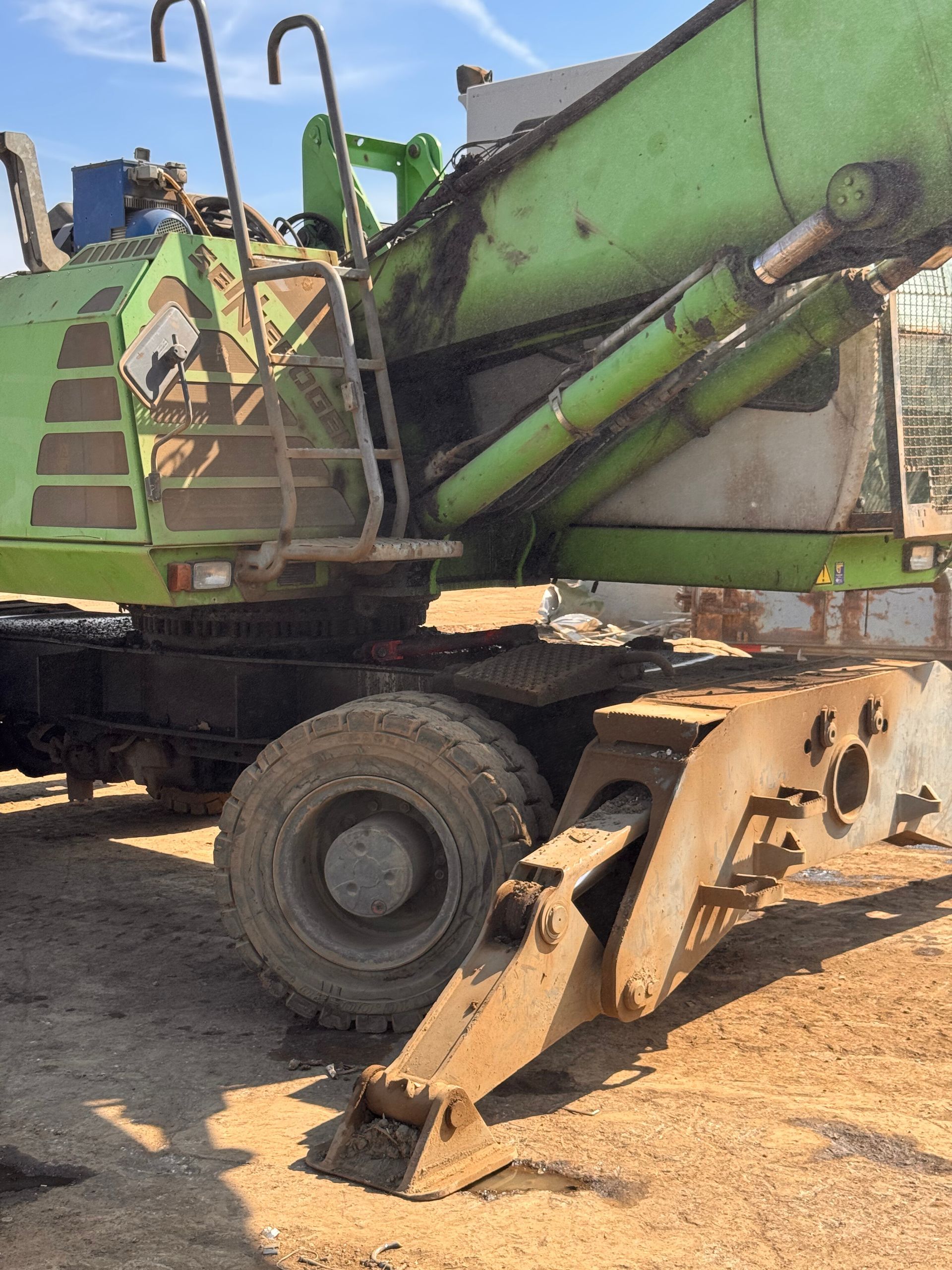 Green cement mixer truck parked on dirt, with rusted chute and large wheels.