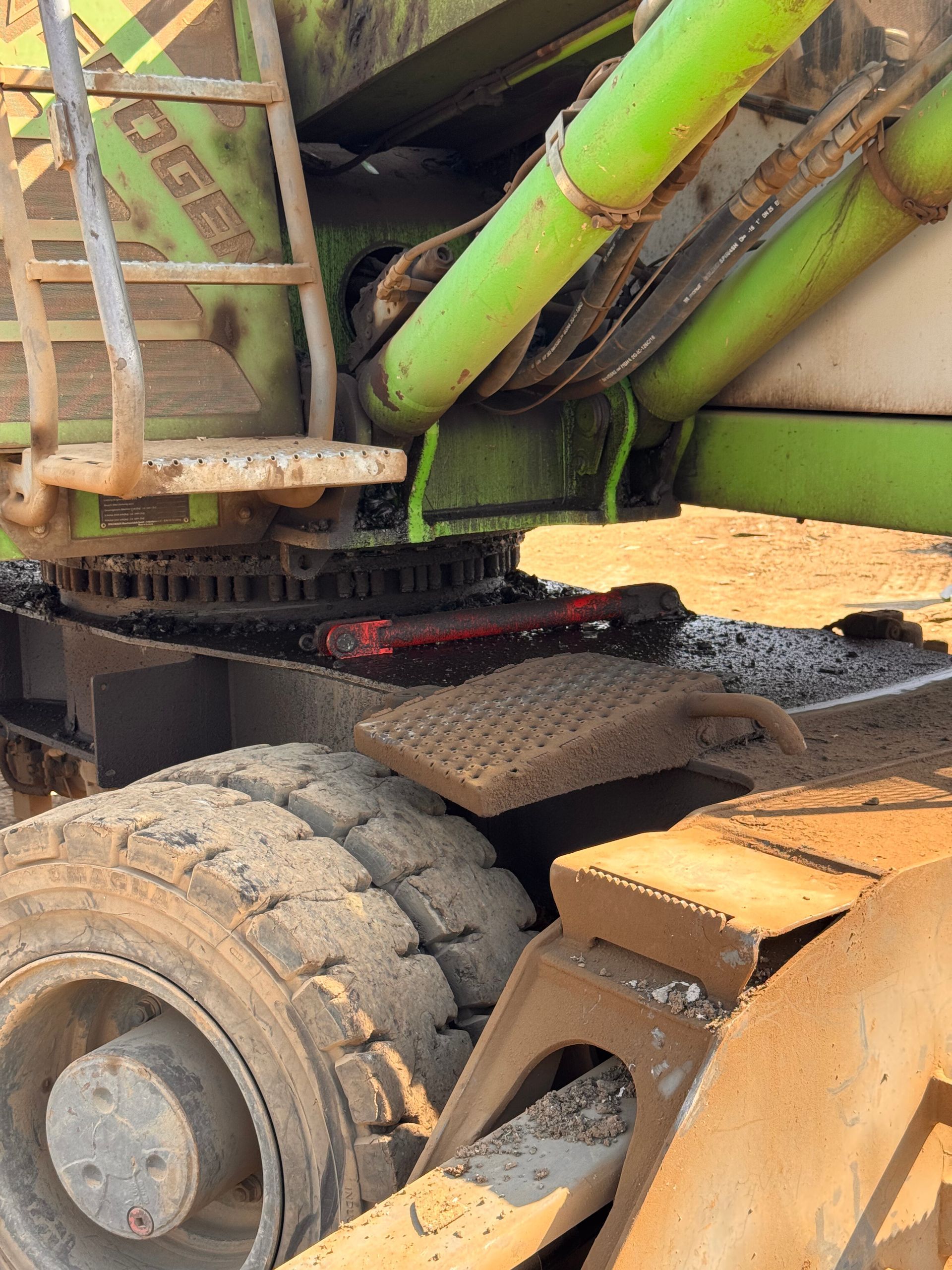 Close-up of a heavy truck’s underside and rear wheels, with green pipes and rusted metal parts.