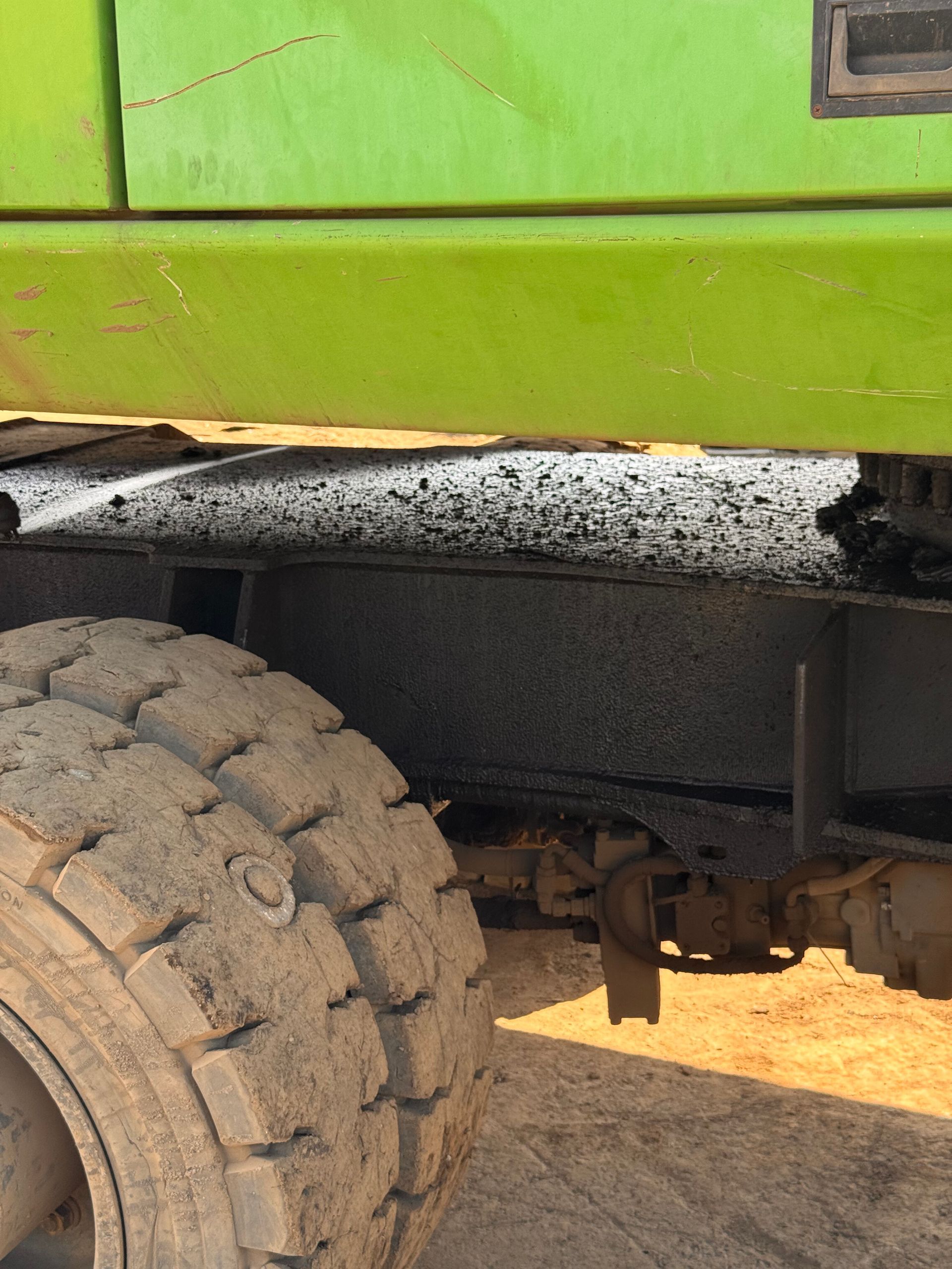 Close-up of a green truck’s side and large tire on a dusty road.