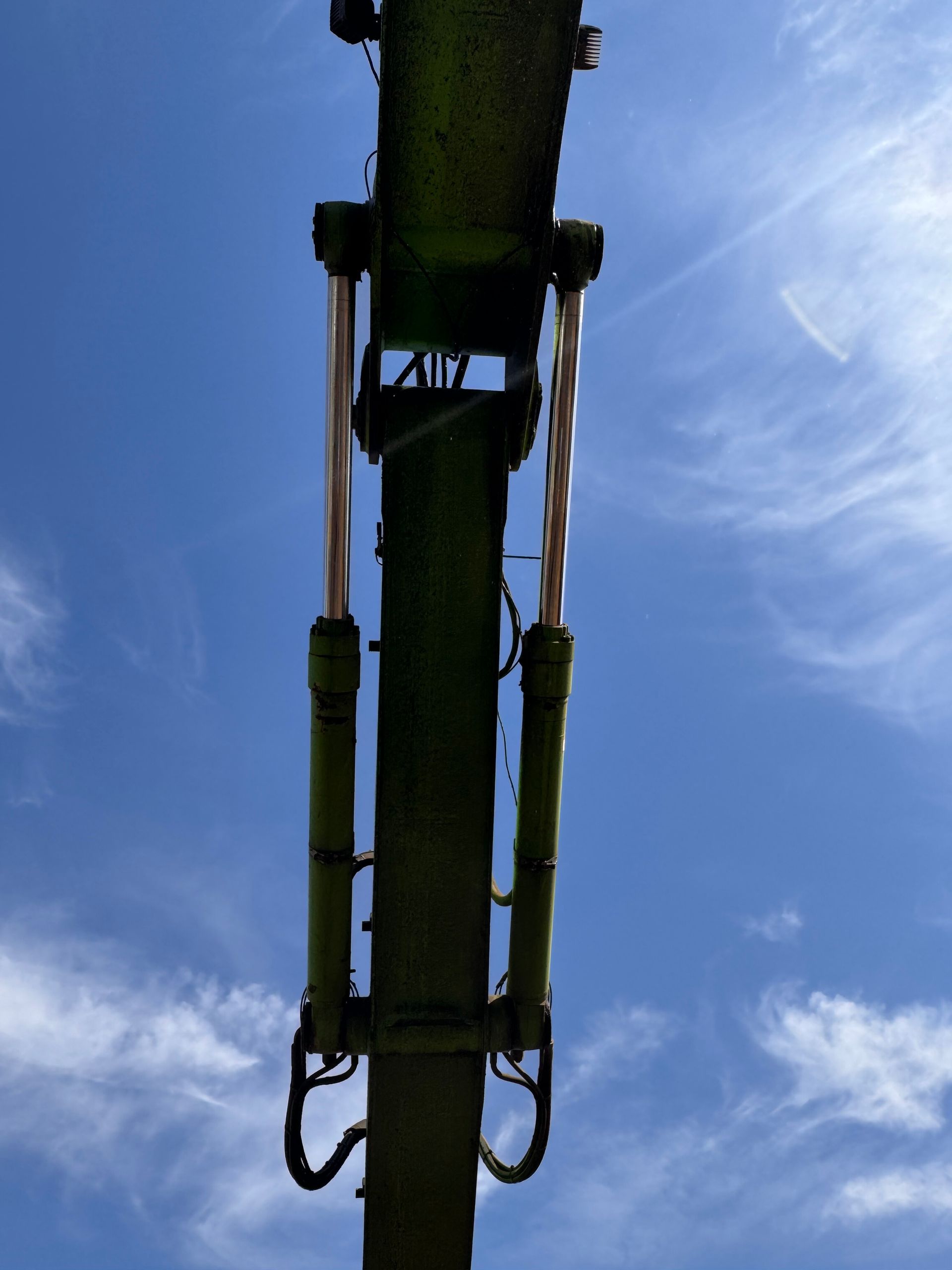 Underside of a green construction boom against a blue sky with clouds