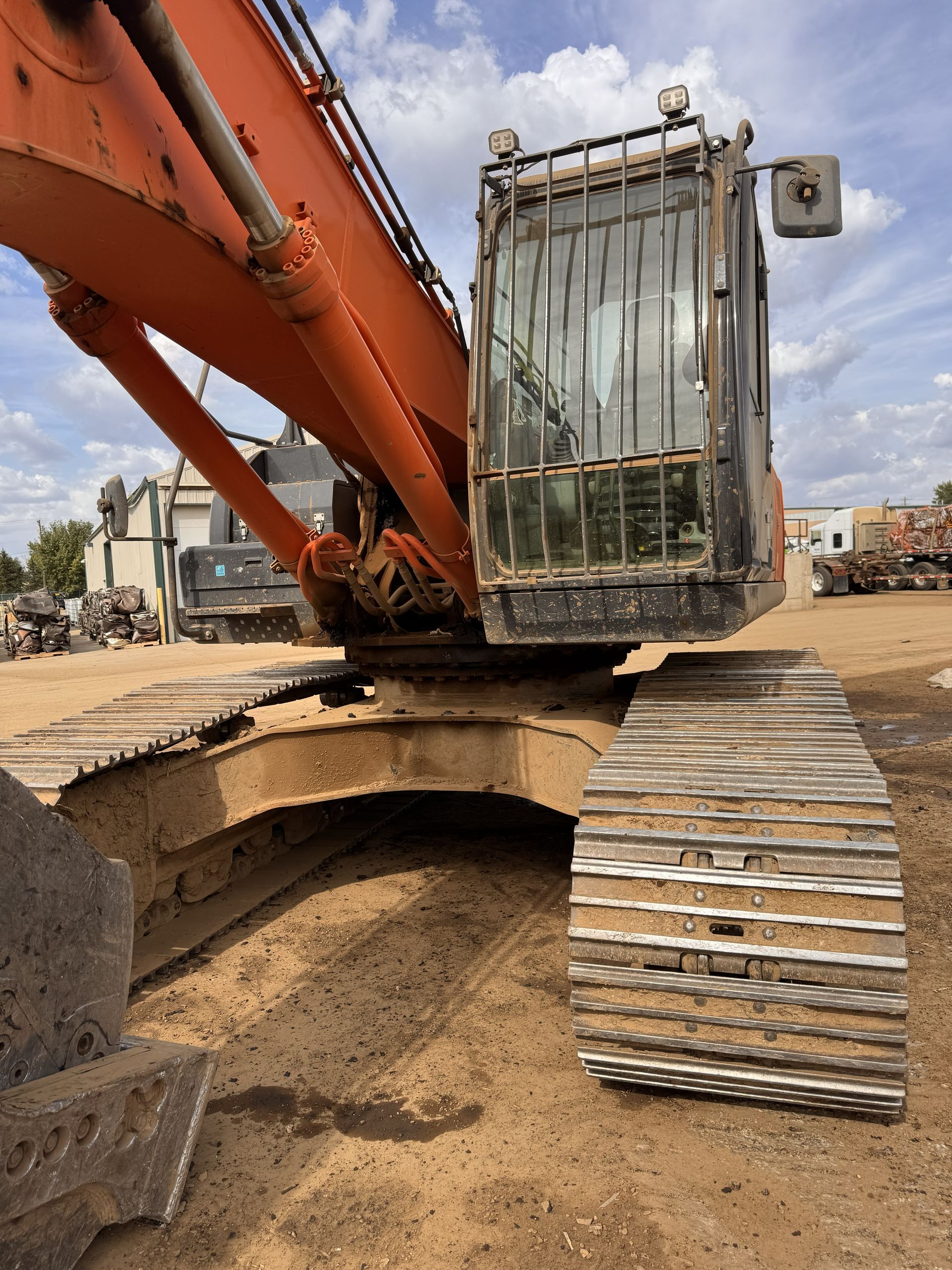 Orange excavator on a construction site with metal tracks and a raised cab.