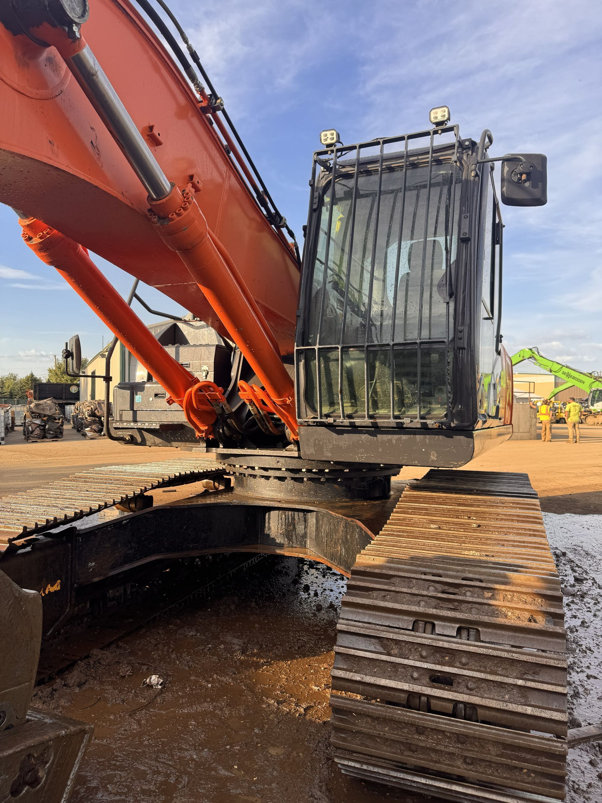 Large excavator lowering a metal cage into a muddy pit at a construction site