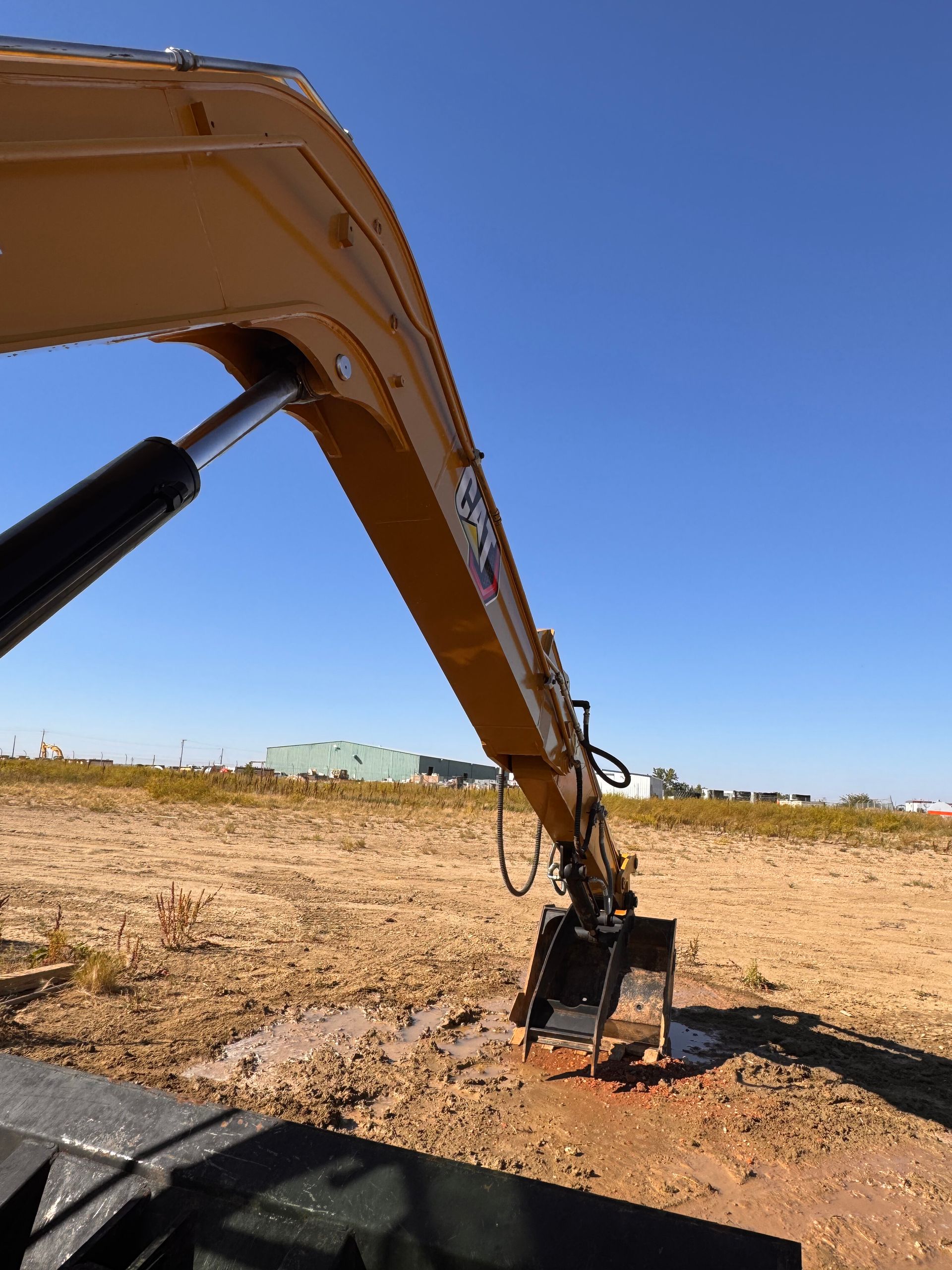 Excavator arm digging in a dry, open field under a clear blue sky
