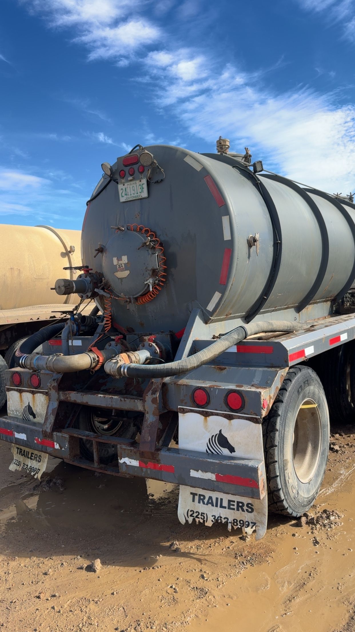 Large gray industrial tanker trailer on a muddy dirt road under a blue sky