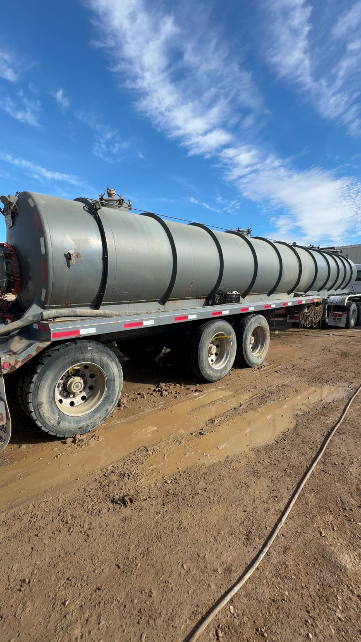 Large silver industrial tank on a trailer in a muddy lot under a blue sky