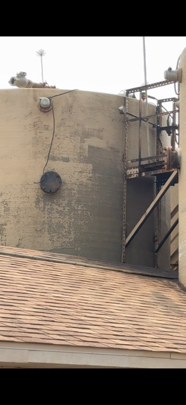 Rooftop utility wall with antennas, pipes, and a metal stairway beside a shingled roof.