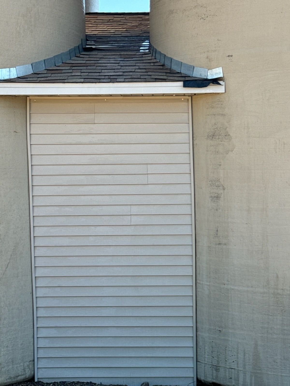 Closed white louvered door beneath a small shingled overhang on a beige stucco wall.