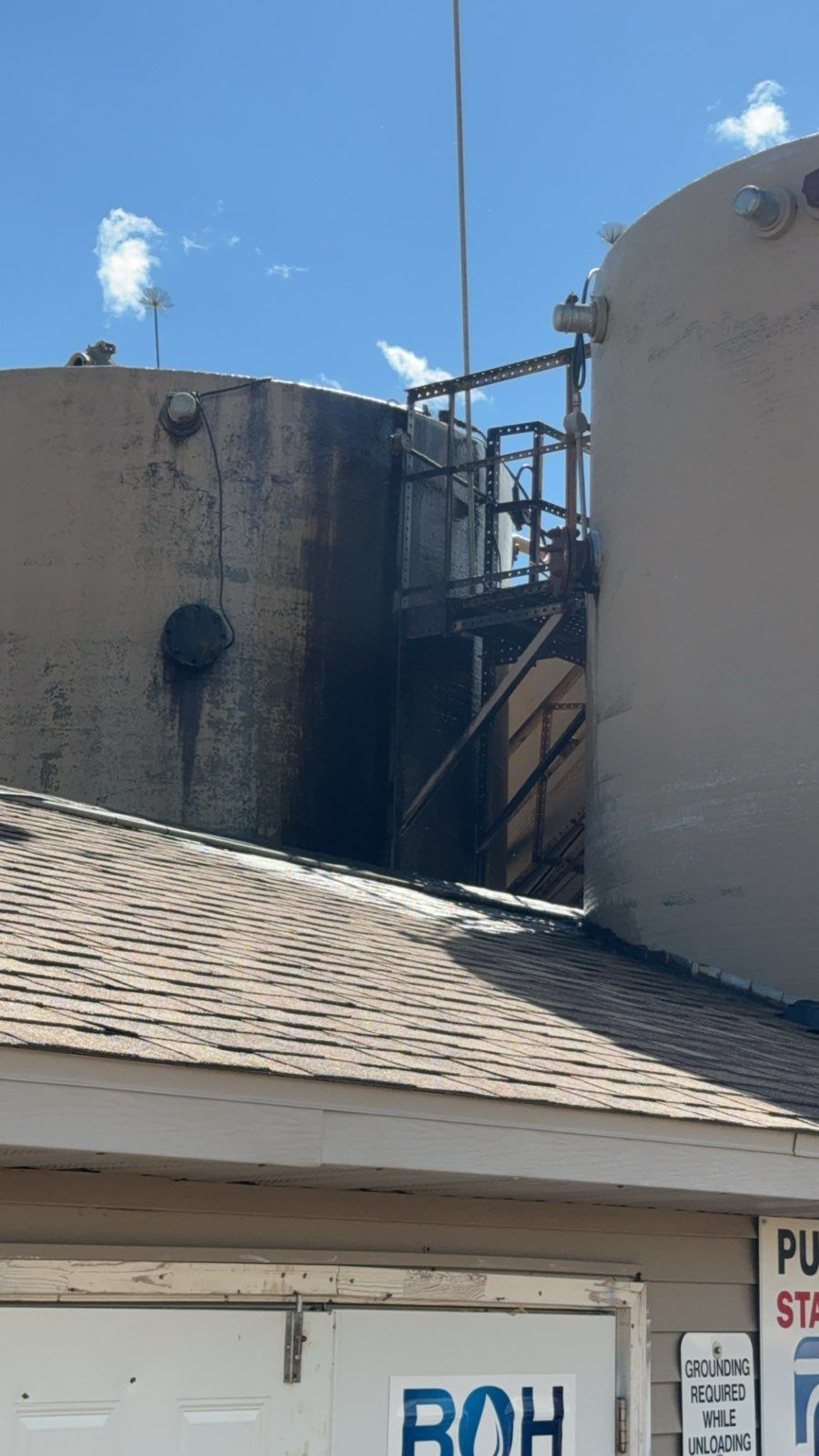 Large white industrial tanks behind a shingled roof under a blue sky