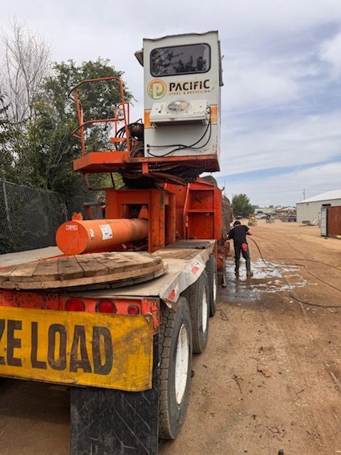 Orange heavy equipment on a flatbed truck on a muddy road, with a worker standing nearby.