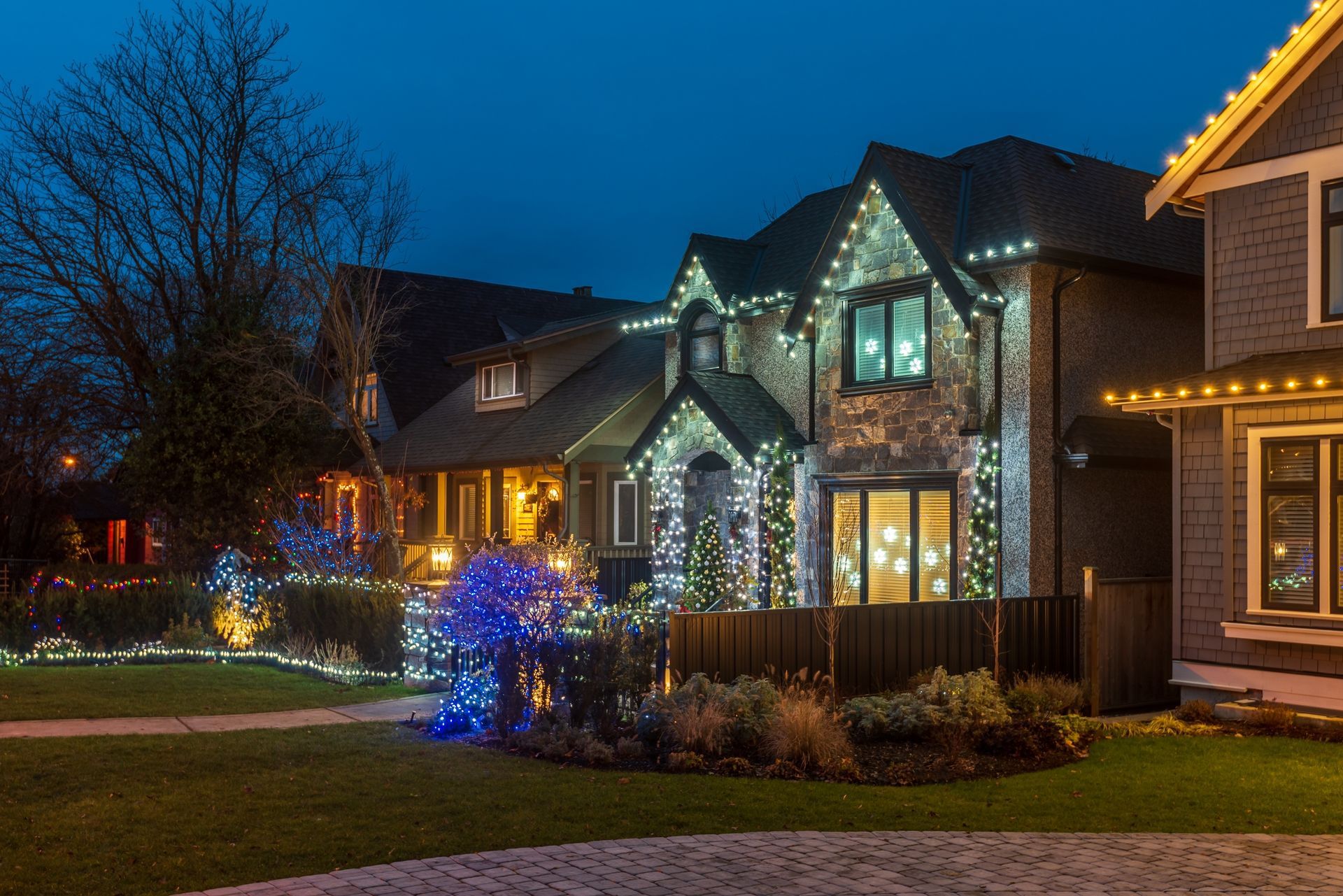 A house decorated with colorful holiday lights at dusk, with a lit walkway and illuminated trees