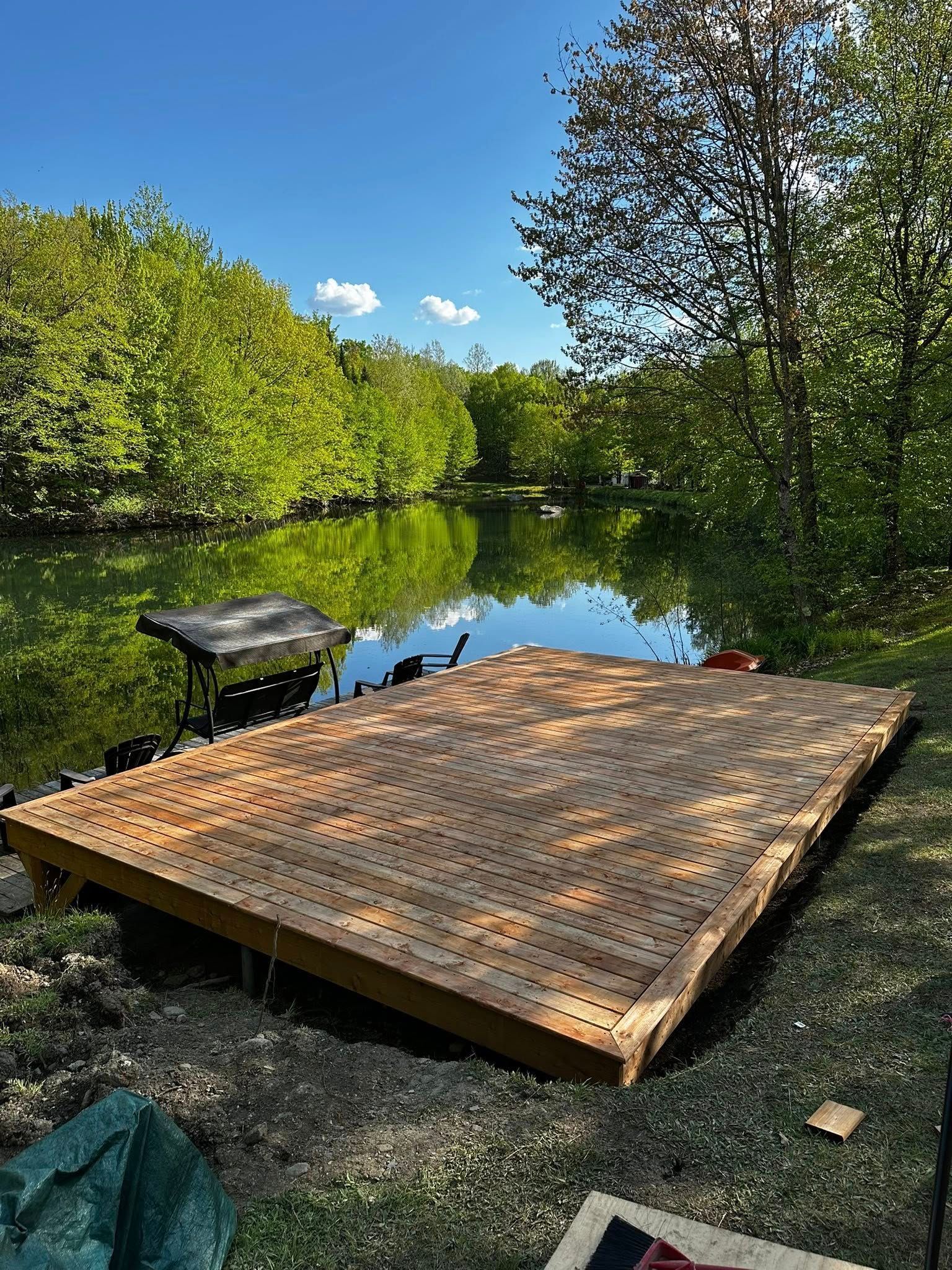 Plateforme de quai en bois au bord d'une rivière calme, entourée d'arbres verdoyants sous un ciel ensoleillé