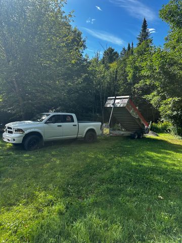 Une camionnette blanche avec une petite remorque garée sur l'herbe à côté d'arbres sous un ciel d'un bleu éclatant