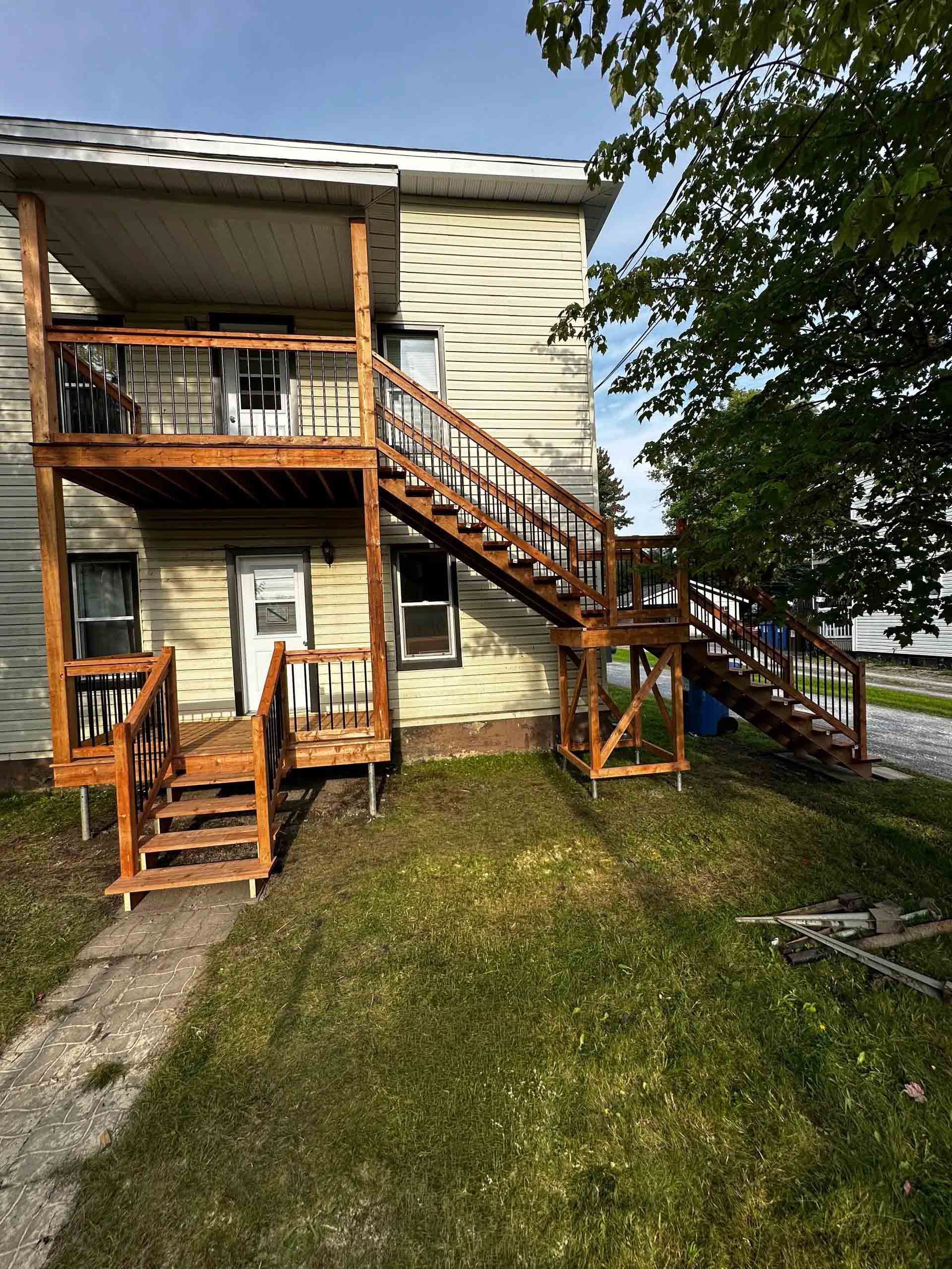 Extérieur d'un immeuble de deux étages avec escaliers en bois, petits balcons et cour gazonnée