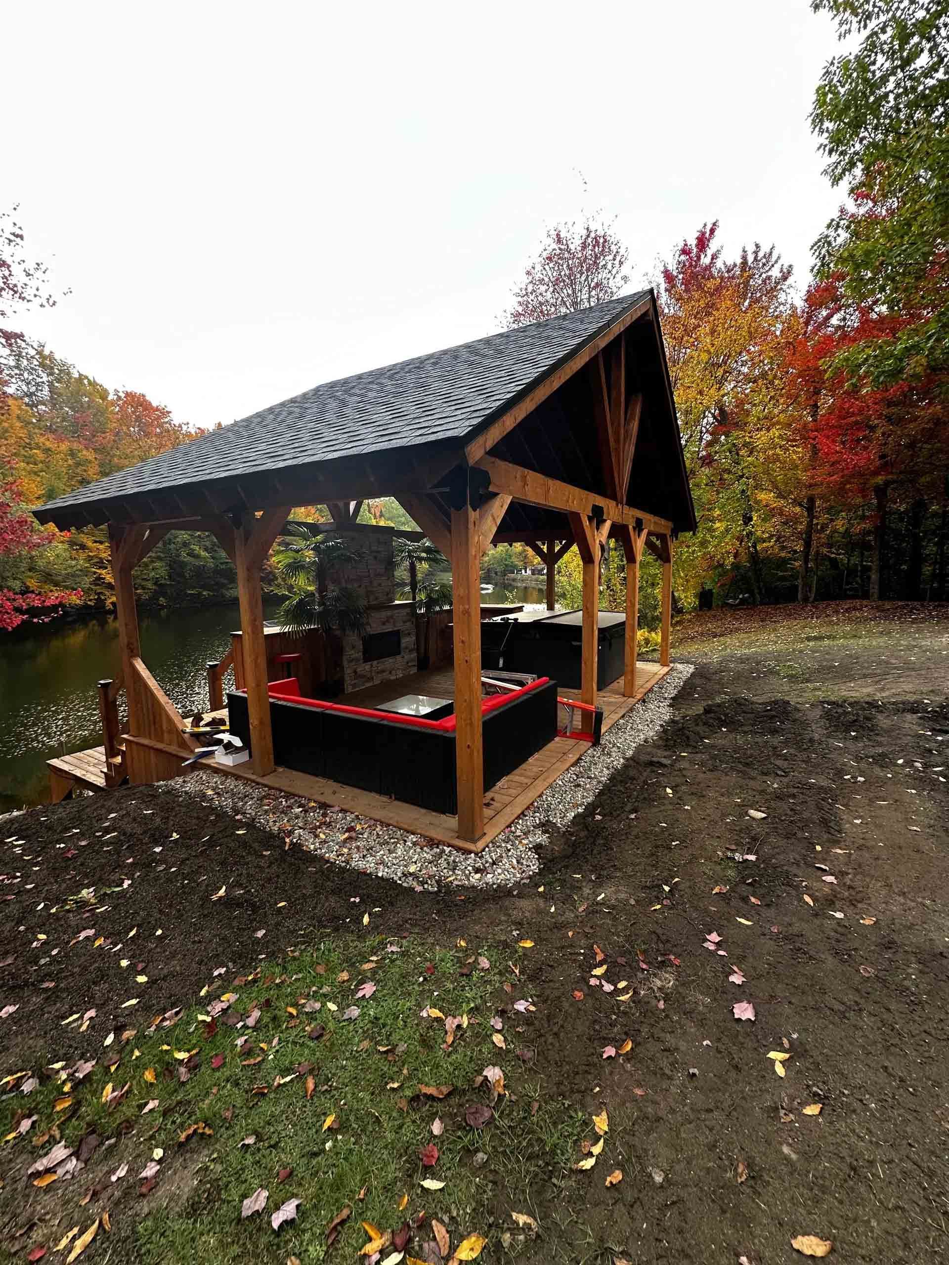 Pavillon en bois au toit de tuiles, situé au bord d'un chemin de terre, entouré d'arbres d'automne et de feuilles mortes.
