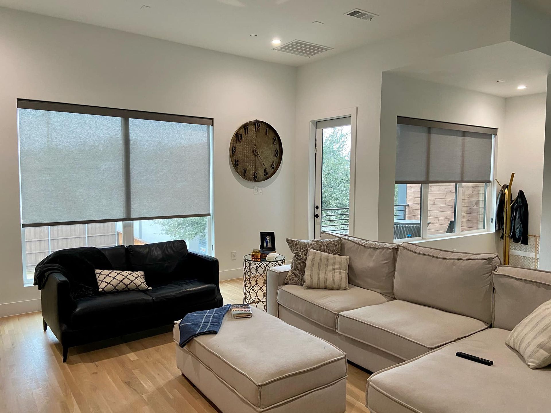 Living room with black and beige sofas, large windows, and a round wall clock.