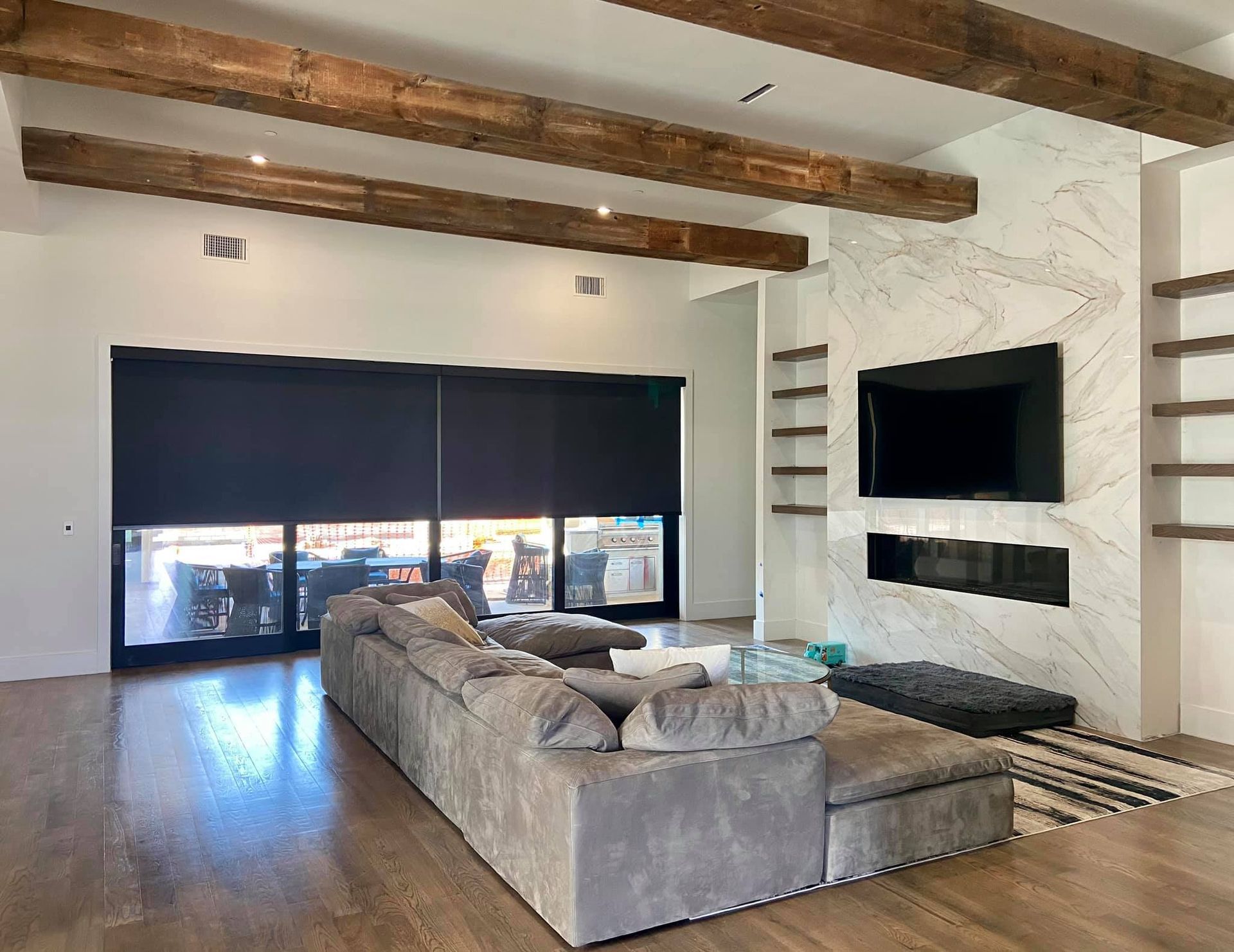 Living room with a large gray sectional, fireplace, TV, and exposed wooden beams.