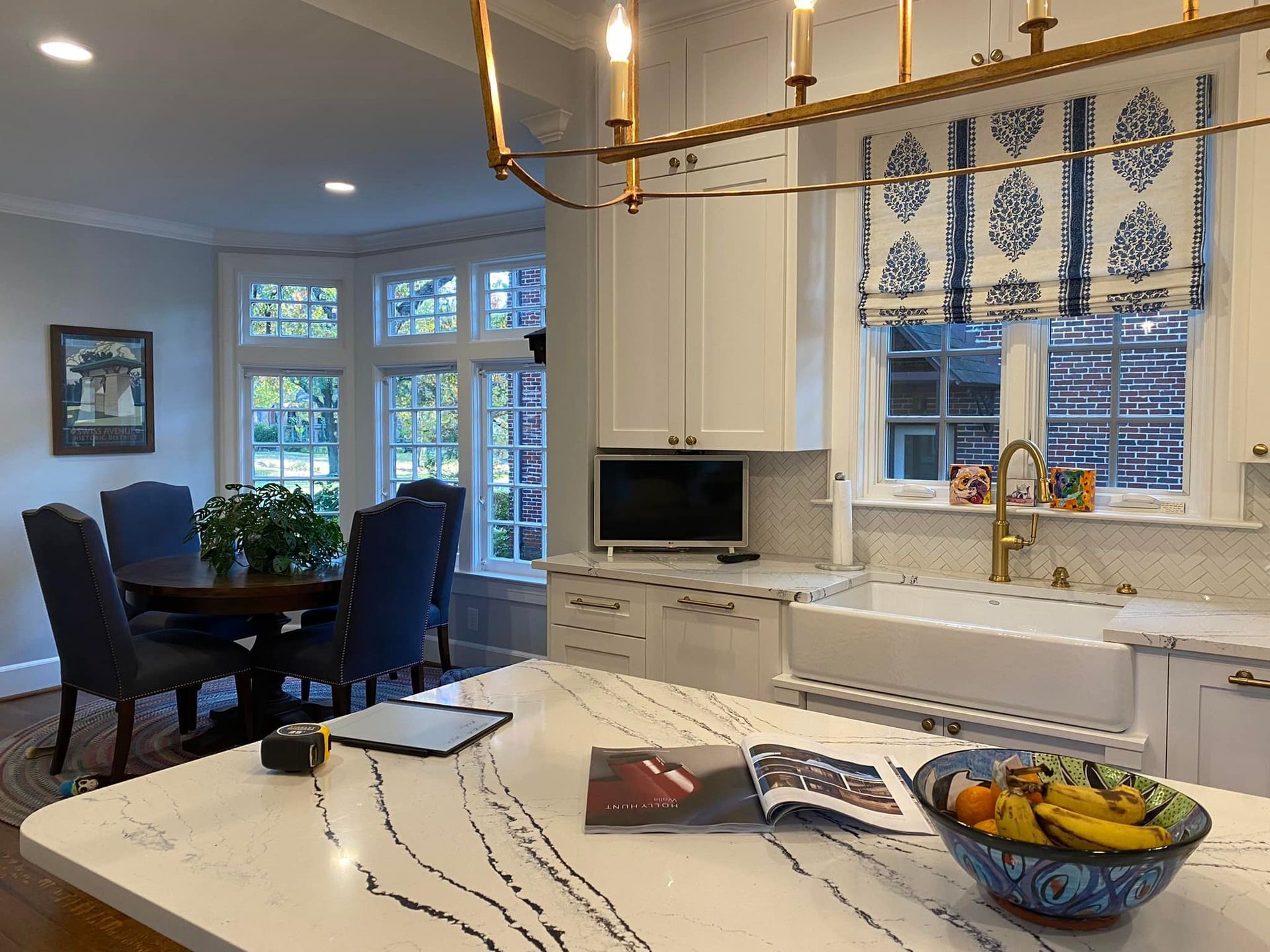 Kitchen with white cabinets, large island, dining area with a round table, and a blue and white patterned window treatment.