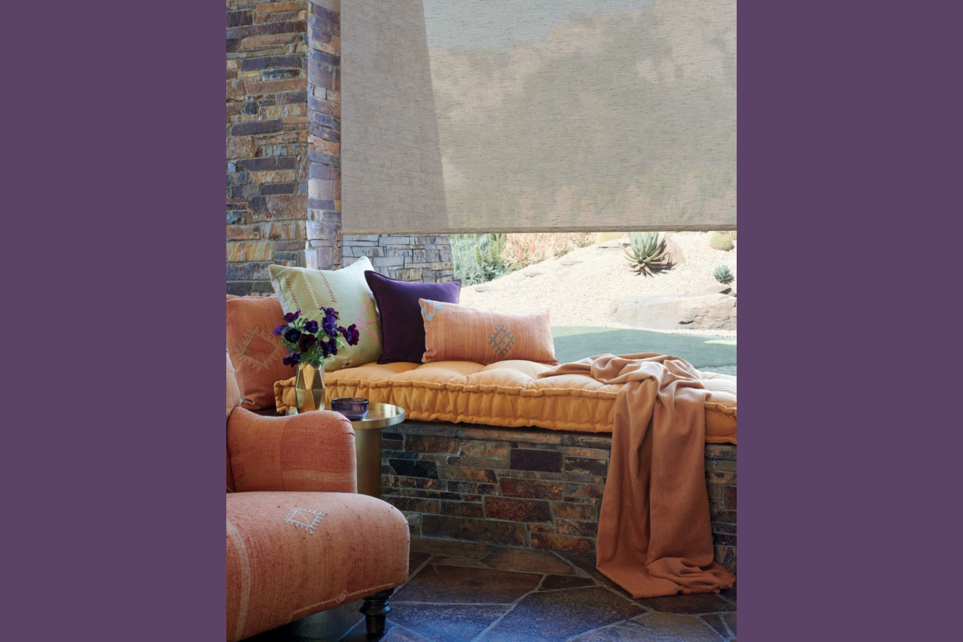 Outdoor seating area with roll-up shade, stone wall, and colorful cushions.