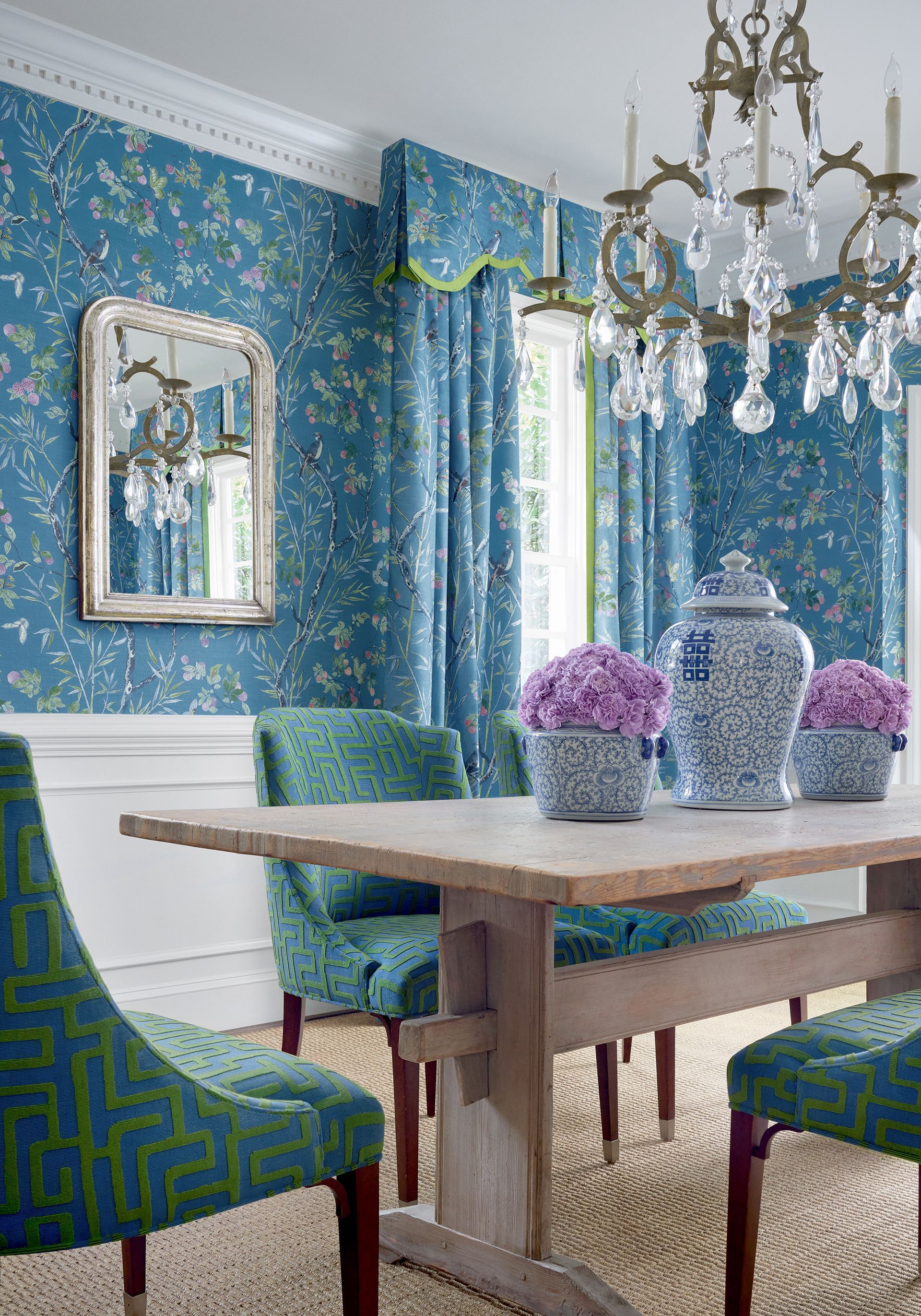 Dining room with floral blue wallpaper, wood table, patterned chairs, and chandelier.