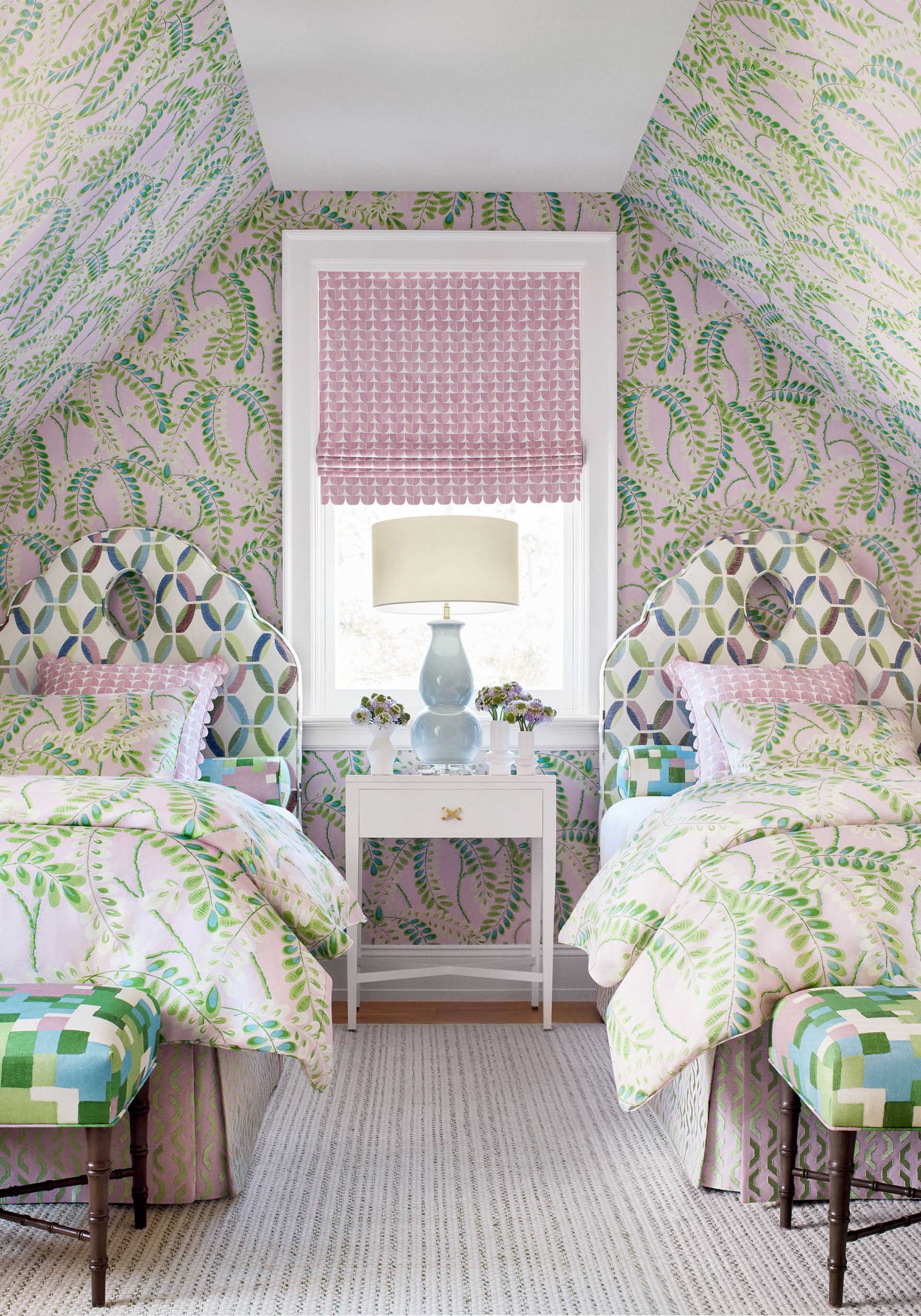 Twin beds in a room with patterned wallpaper, matching headboards, and a window with pink shade.