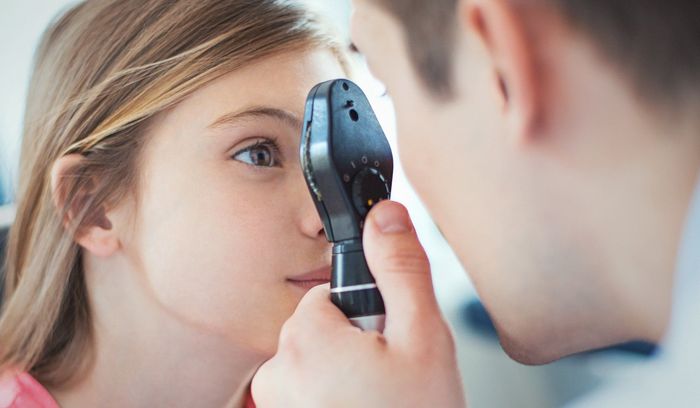 Primo piano di una visita oculistica: un medico utilizza un oftalmoscopio sull'occhio di una donna.