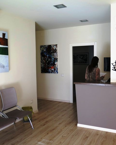 Ufficio moderno con pavimento in legno, opere d'arte alle pareti, una sedia e una persona in piedi dietro un bancone della reception.