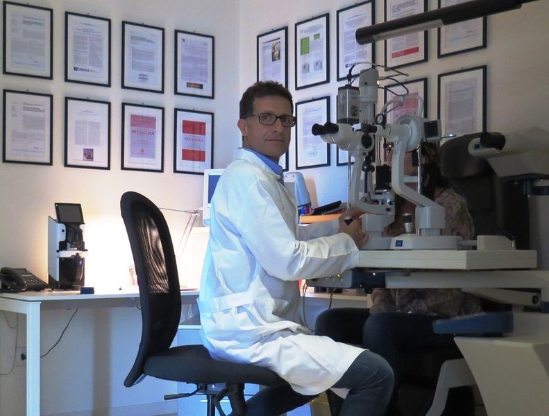 Scienziato seduto davanti a un microscopio in un luminoso ufficio con certificati incorniciati alle pareti.