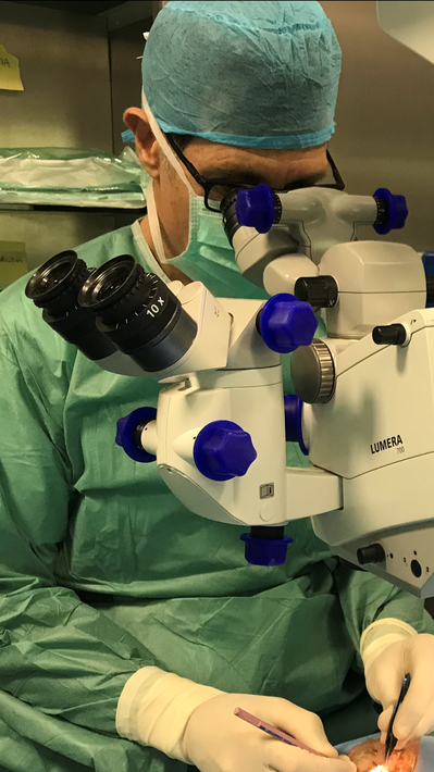 Chirurgo in camice verde che utilizza un microscopio durante un intervento agli occhi.