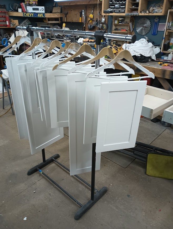 White cabinet doors drying on a hanging rack in a workshop setting.