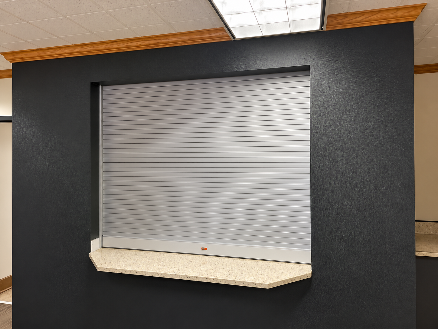 Closed service window with metal shutter and small ledge in an indoor office or lobby area