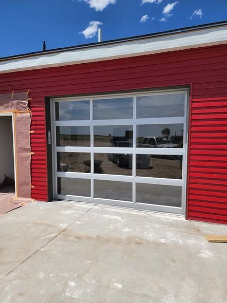 Red building exterior with a large glass garage door and concrete driveway under a blue sky