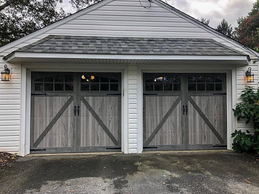 Gray double garage doors on a white house with a shingled roof and driveway in front
