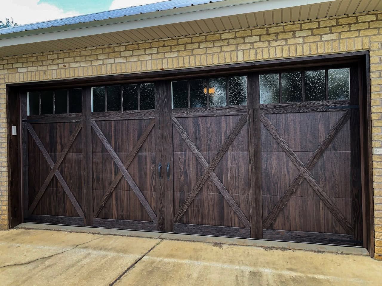 Dark wooden garage door with X-braced panels under a tan brick house facade