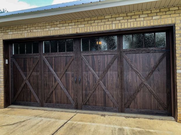 Dark wooden garage doors with diagonal bracing beneath a tan brick exterior.