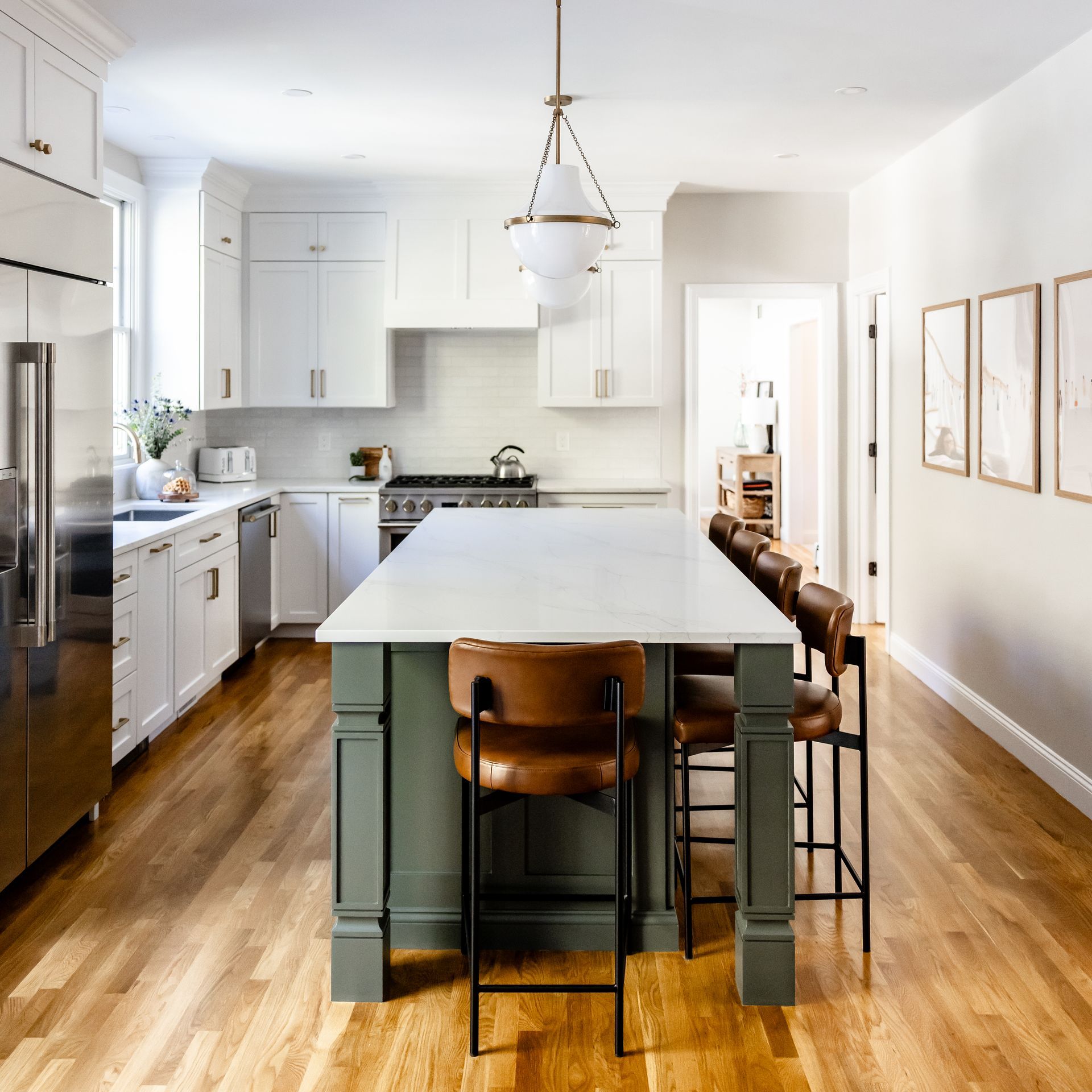 Bright modern kitchen with large island, white cabinets, wood floors, and bar stools