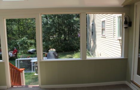 Covered porch with large windows overlooking a green backyard and neighboring house.