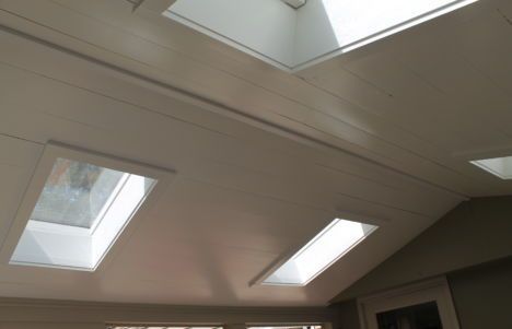 White vaulted ceiling with three skylights and recessed lights in a bright room