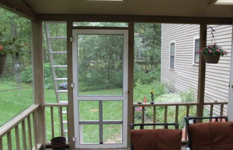 Screened porch overlooking a green backyard, with a door, railings, and hanging flower basket.